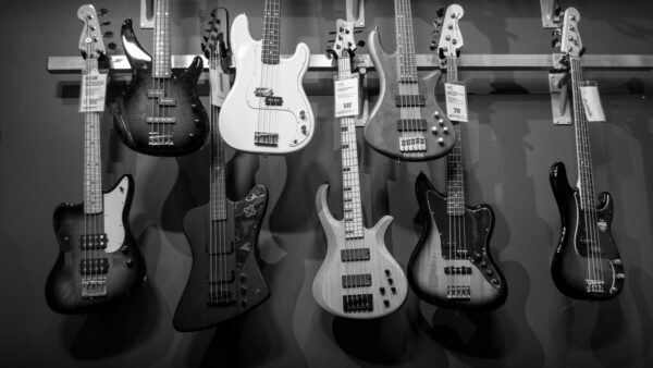 Black and white display of various electric bass guitars hanging on a rack.